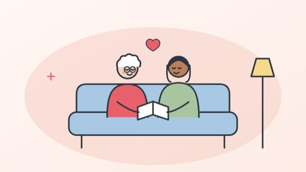 Live in carer reading a book with an older woman on the sofa at home